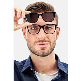 Een man met een zwarte leesbril die een zonnebril clip-on boven de bril houdt, vooraanzicht.