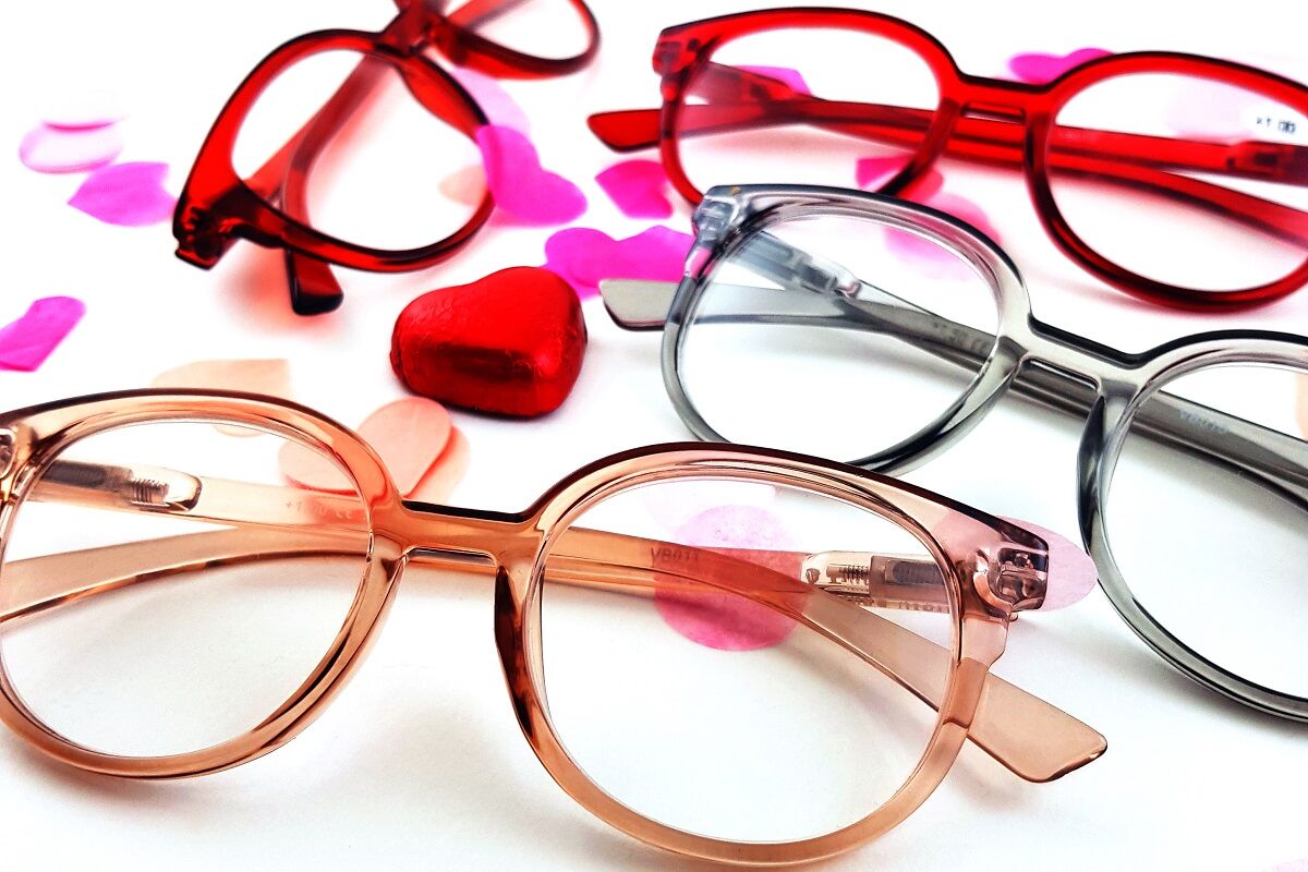 Een aantal leesbrillen in tinten roze en rood op een witte tafel met hartjes.